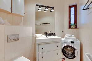 Ein kleines Badezimmer mit Waschmaschine, Beleuchtung am Spiegel und einem kleinen Fenster.