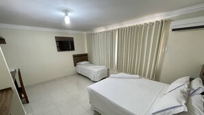Une chambre d’hôtel avec deux lits simples, un téléviseur à écran plat fixé au mur et un ventilateur de plafond.