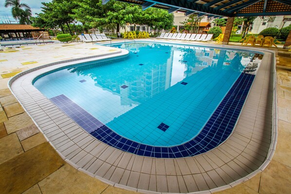 Una piscina con bordes de azulejos, rodeada de sillas de descanso y una zona cubierta.