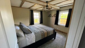 Un dormitorio con una cama, ventilador de techo y dos ventanas con cortinas.