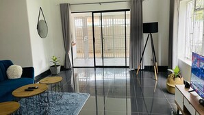 Un salon moderne avec un canapé bleu, une table basse, un téléviseur et un balcon offrant une vue agréable.
