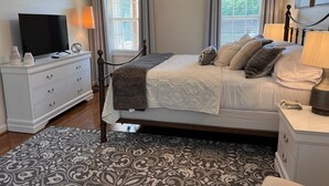 A neatly arranged bedroom with a bed, bedside tables, a TV, and a patterned rug. - Cozy home near RDU, RTP, Angus Barn & downtown! Pet Friendly! Level-2 EV Charger (Raleigh)