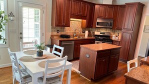 A kitchen with wooden cabinets, a granite countertop island, white chairs, and a dining table. - Cozy home near RDU, RTP, Angus Barn & downtown! Pet Friendly! Level-2 EV Charger (Raleigh)