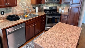 A kitchen with dark wooden cabinets, a stainless steel dishwasher, a gas stove, and a microwave. - Cozy home near RDU, RTP, Angus Barn & downtown! Pet Friendly! Level-2 EV Charger (Raleigh)