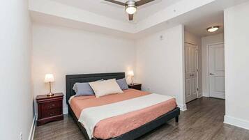 Une chambre à coucher avec un lit, deux tables de chevet, un ventilateur de plafond et une porte.