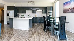Uma cozinha moderna com ilha central, eletrodomésticos de aço inoxidável e área de jantar com mesa e cadeiras de vidro.