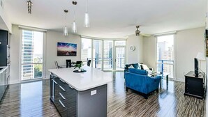 Apartamento moderno com ilha de cozinha, sofá azul e grandes janelas com vista para a cidade.