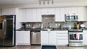 Een moderne keuken met witte kastjes, roestvrijstalen apparatuur, een vaatwasser, een spoelbak en een magnetron.