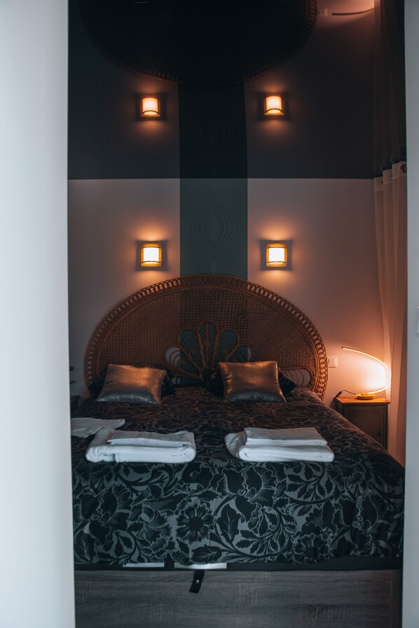 Un lit avec une tête de lit en osier, deux lampes fixées au mur et une table de chevet avec une lampe.
