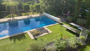 Una piscina envoltada d'un jardí ben cuidat, una cadira lluent i una vista al camp.