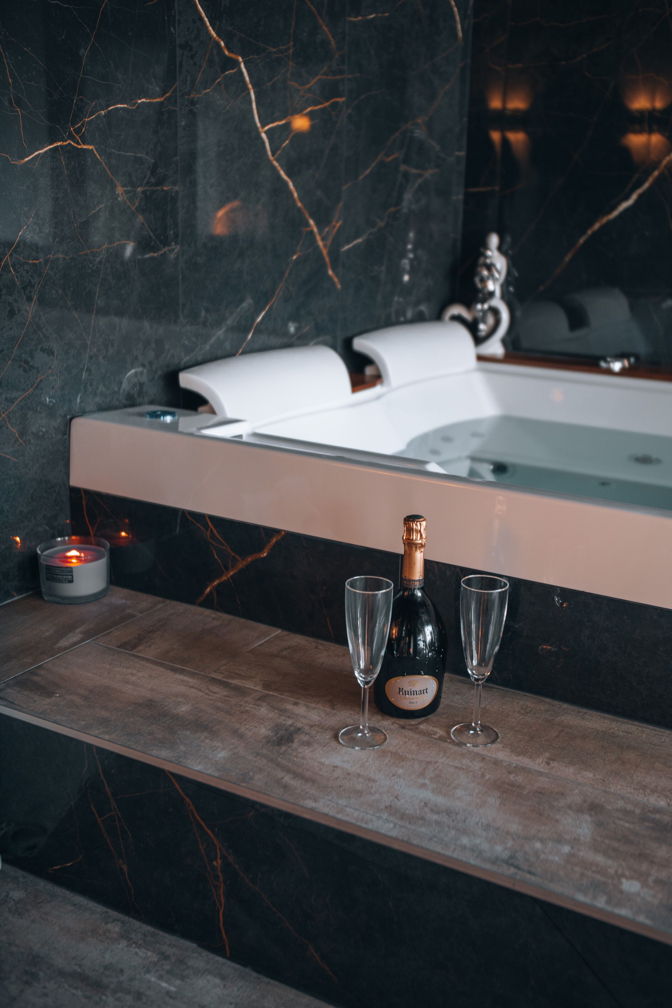 Un baño con suelo de mármol, una bañera, una botella de champán Ruinart y dos copas de champán.