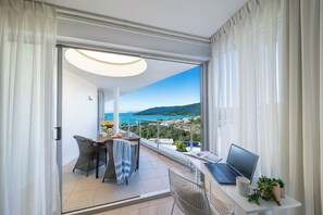 A balcony with a laptop, a table with chairs, and a view of the sea and hills.