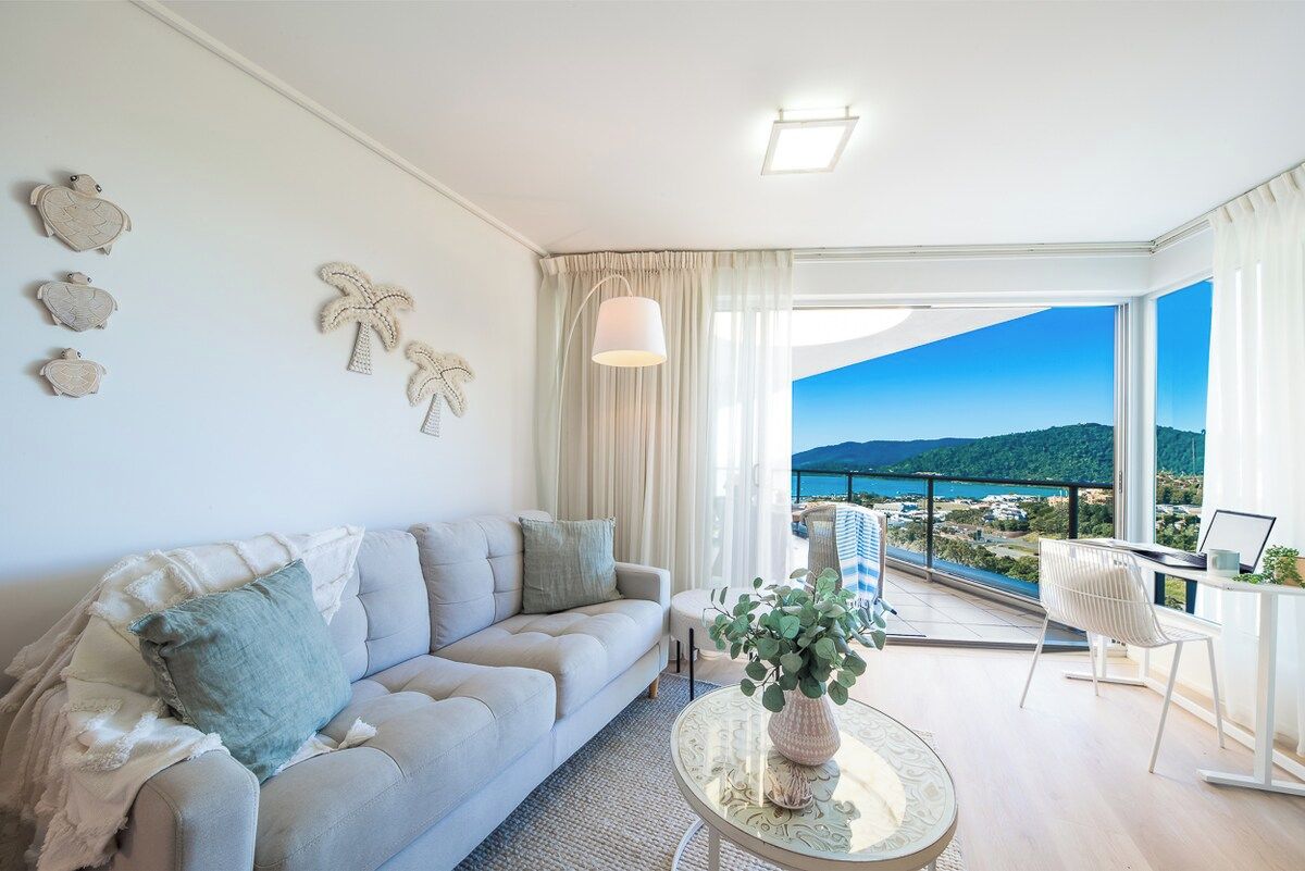 A modern living room with a sofa, a coffee table, and a view of the sea.