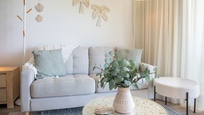 Una sala de estar con un sofá, una mesa redonda de centro con una planta y decoración en la pared.