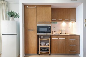 A compact kitchen with wooden cabinets, a built-in microwave, a sink, and a small shelf unit.