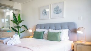 Una cama bien hecha con un cabecero gris, dos lámparas de noche y una mesita de noche con lámpara.