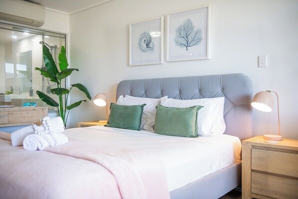 A neatly made bed with a grey headboard, two bedside lamps, and a bedside table with a lamp.