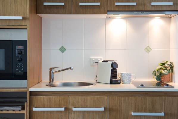 A modern kitchen with wooden cabinets, a stainless steel sink, a microwave, and a coffee maker. - Stunning One Bedroom Apartment With Ocean Views (Airlie Beach)