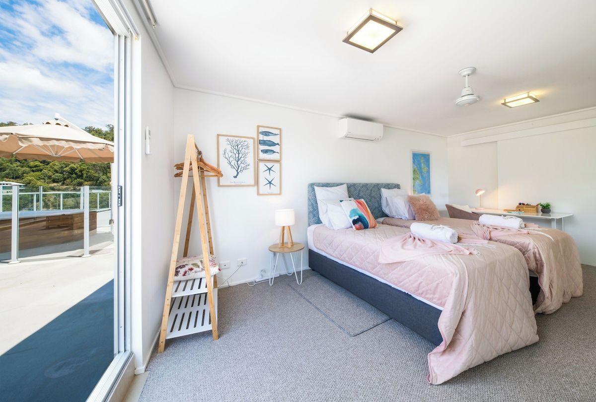 A bedroom with a large bed, a ladder, a small table, and a view of the outdoors.