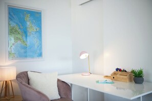 Ein Zimmer mit einem weißen Schreibtisch, einer Karte an der Wand, einer Lampe, einem Stuhl und einer Pflanze.