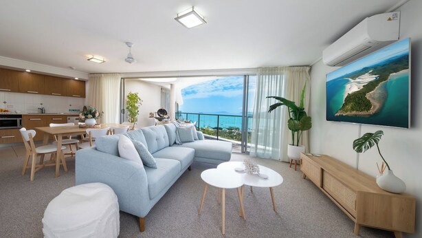 En moderne stue med sofa, sofabord og spiseplads, med et stort vindue der ud til havet.
