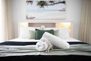 A neatly made bed with a rolled white towel and a decorative item on the bed.