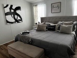 A modern bedroom with a large bed, a bedside table, a tray, and a wall art piece.
