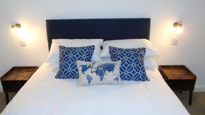 A neatly made bed with a dark headboard, two bedside tables with lamps, and a world map pillow. - Snug - Sealladh Mara Apartment (Helensburgh)