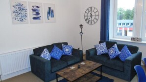 A room with two dark grey sofas with patterned cushions, a wooden coffee table, and a wall clock. - Snug - Sealladh Mara Apartment (Helensburgh)