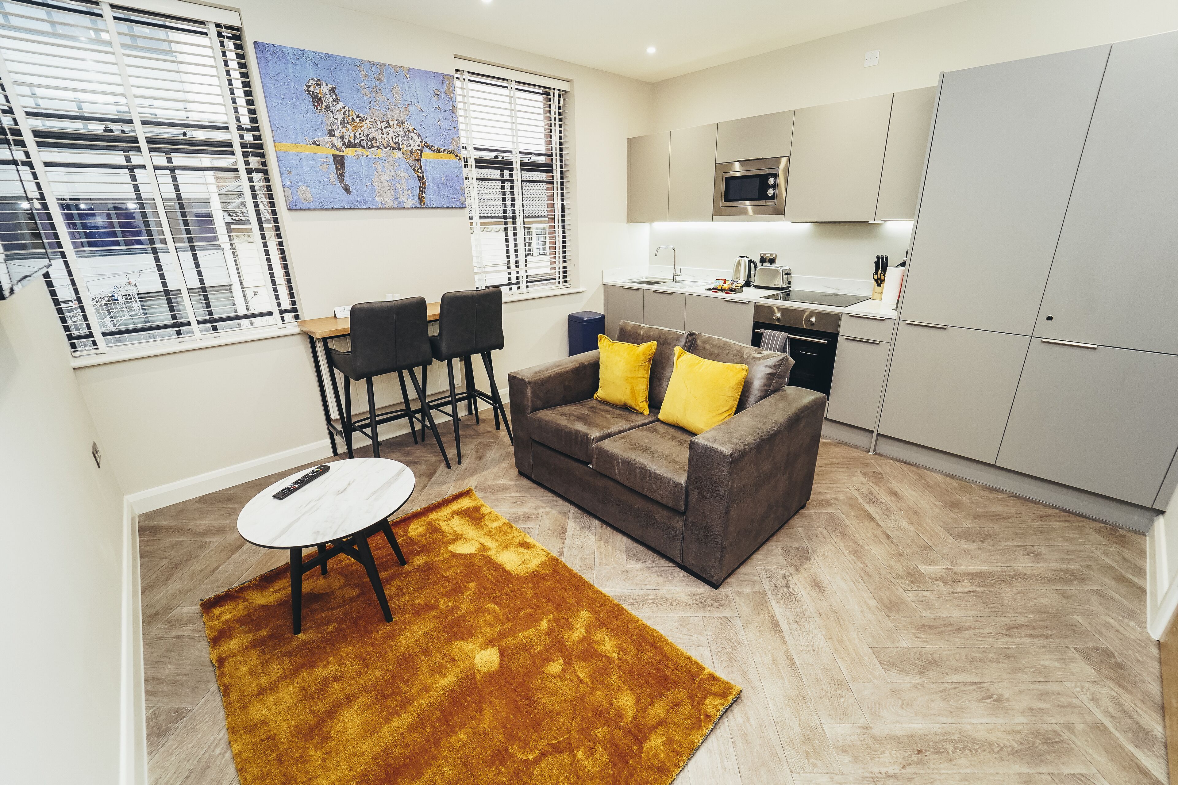 Een moderne woonkamer met een grijze bank, gele kussens, een witte salontafel en een bruin vloerkleed.