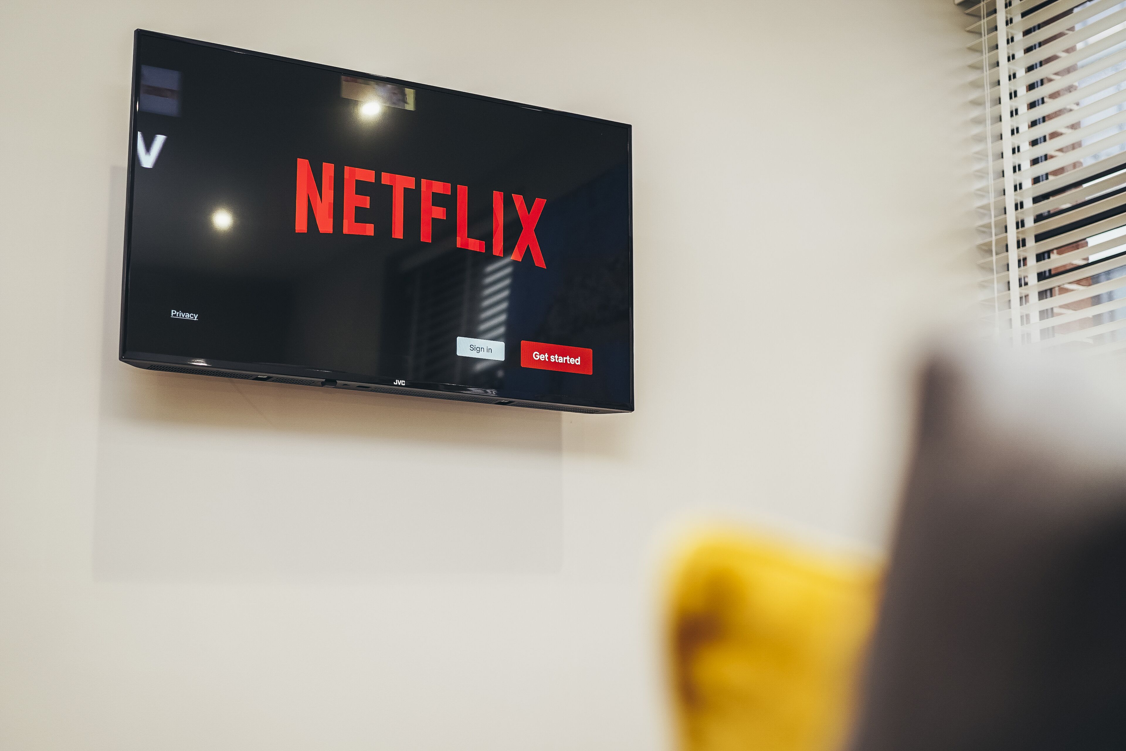 A flat-screen TV mounted on a wall displaying the Netflix logo with 'Sign in' and 'Get started' buttons.
