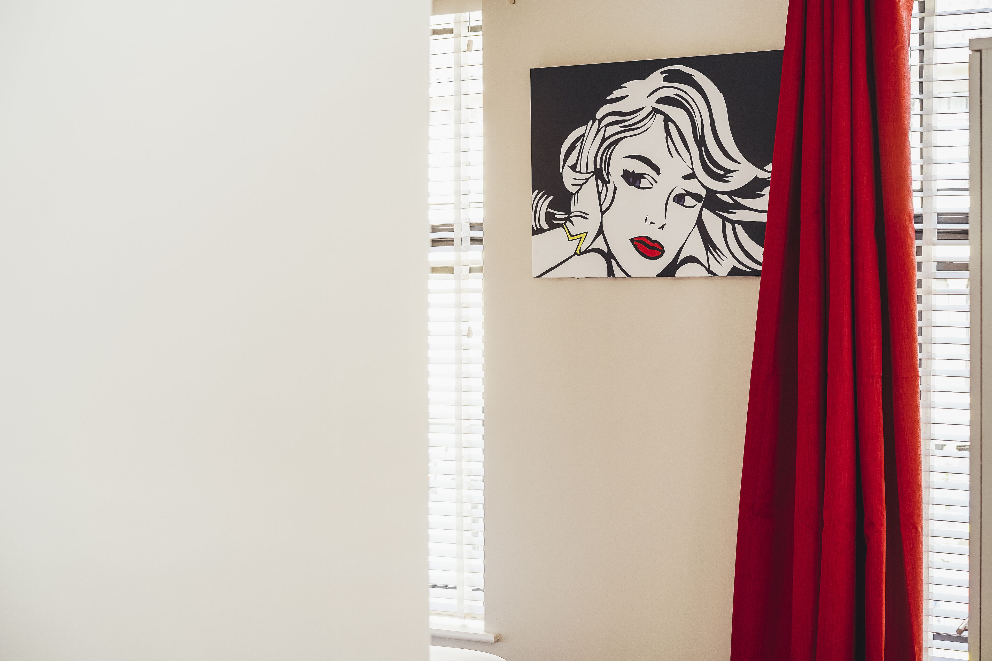 Una habitación con ventana, una cortina roja y una obra de arte blanco y negro en la pared.