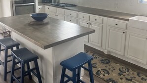A kitchen with white cabinets, a large island with stools, a microwave, an oven, and a window with natural light. - Relax and Unwind in a Home overlooking Lake Texoma (Kingston)
