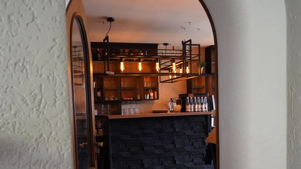 Vista del interior de un bar, con mostrador de piedra, suelo de madera y luces colgantes.