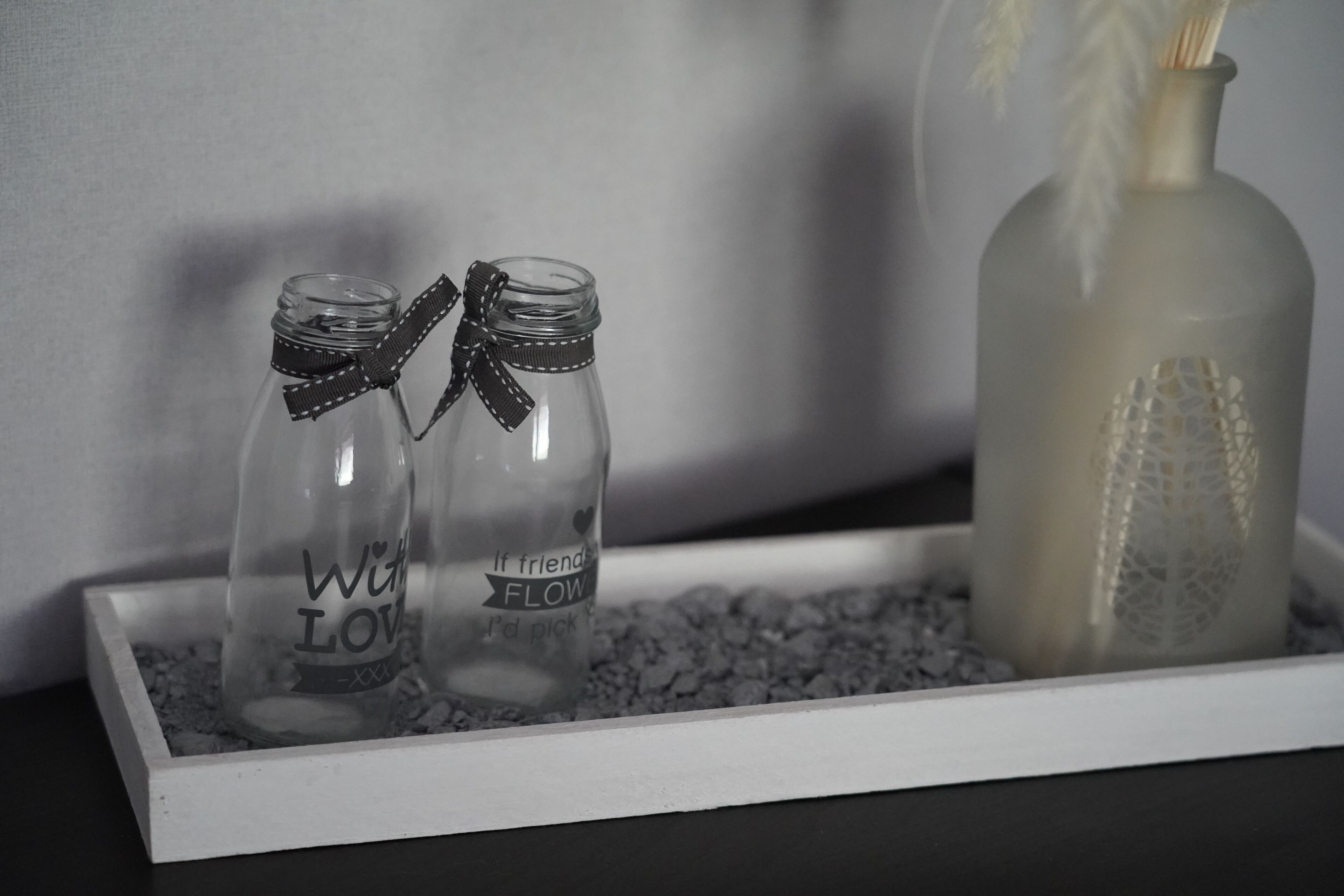 Zwei klare Glasflaschen mit Schleifen, platziert auf einer Schale mit kleinen Kieselsteinen.