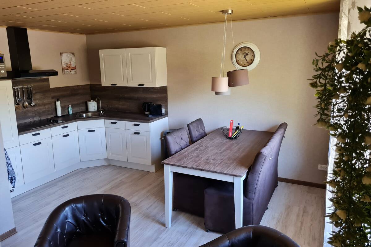 Een moderne keuken met witte kastjes, een houten aanrecht en een zithoek met tafel en stoelen.