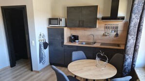 Cocina compacta con microondas, pileta y placares. Hay una mesa redonda con dos sillas y un objeto decorativo sobre ella.