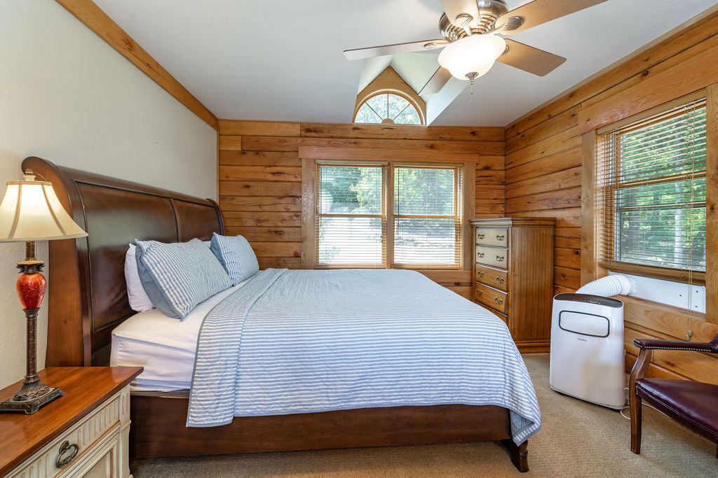 A bedroom with a wooden ceiling, a bed with a striped bedspread, a nightstand with a lamp, a dresser, and a heater.