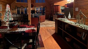 A cozy log cabin interior with a dining area, kitchen, and a large window. - 5BR Table Rock Lake Getaway |Hot Tub, Pool Games (Blue eye)
