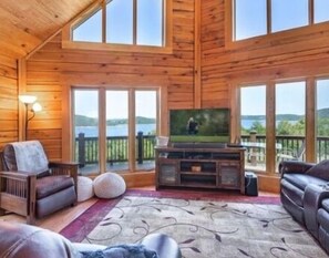 Interior acogedor de una cabaña con una televisión grande, paredes de madera y vistas a un lago pintoresco.