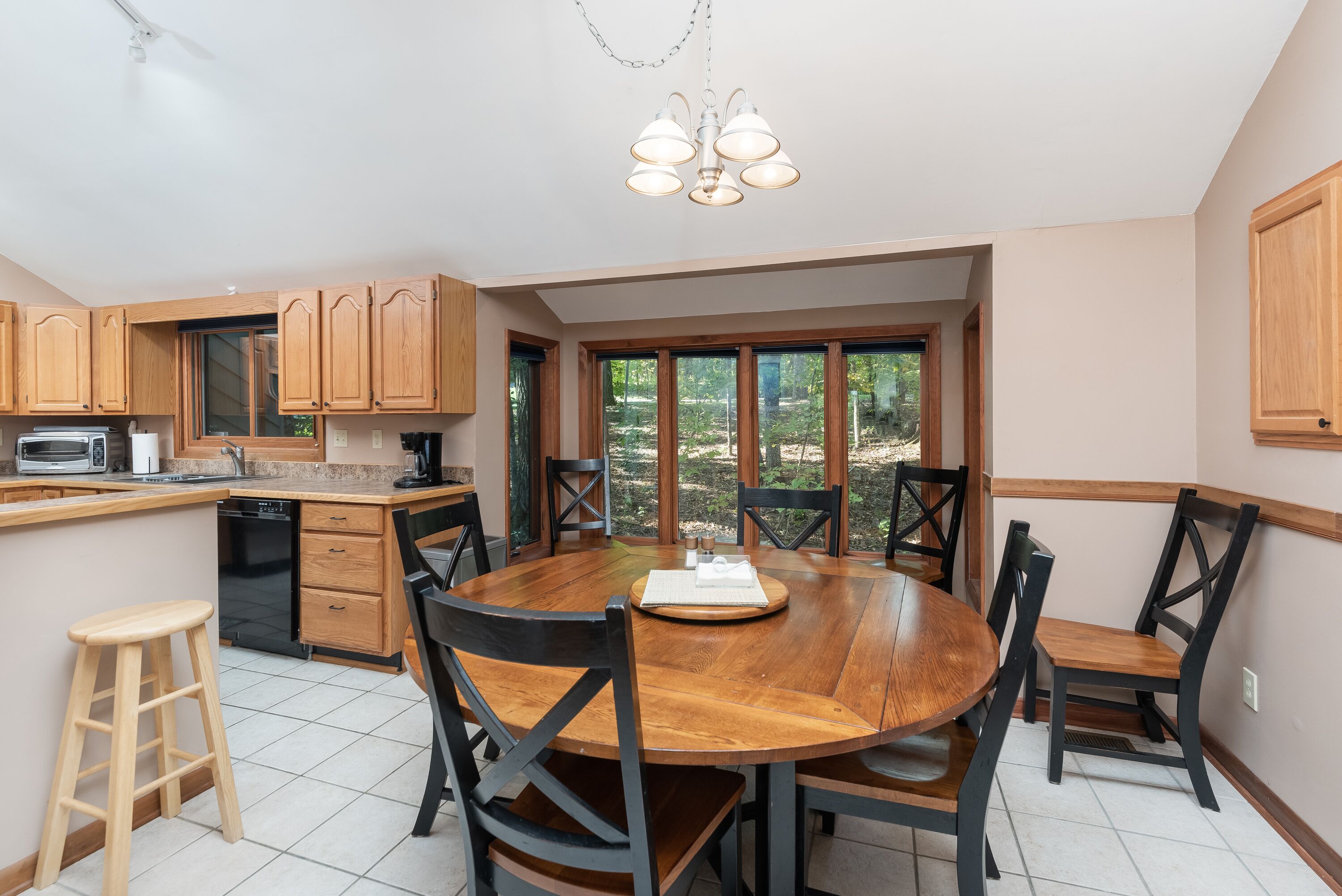 A kitchen with wooden cabinets, a round dining table, and chairs. There is a window with a view of trees.