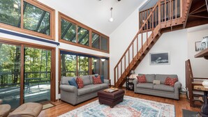A spacious living room with a large window, a wooden staircase, and a gray sofa set.