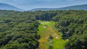 A golf course surrounded by dense forest and mountains.