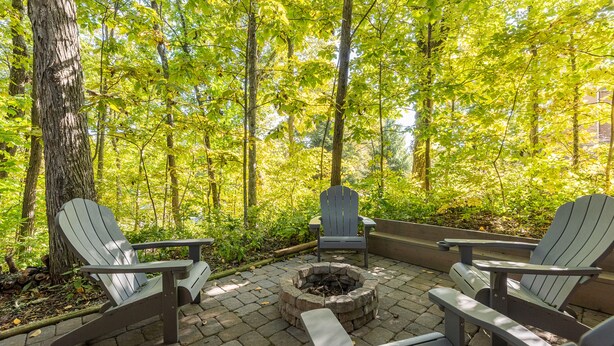 A patio with Adirondack chairs and a fire pit surrounded by a forest.