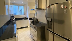 A modern kitchen with stainless steel appliances, a black countertop, and a view of the outside through large windows.