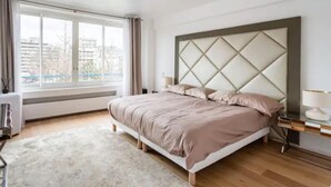 A modern bedroom with a large bed, a window with curtains, a bedside table, and a nightstand.