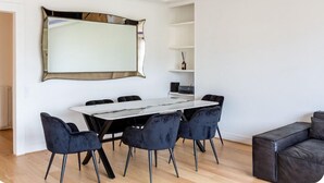 A modern living room with a marble-topped dining table, black velvet chairs, a large mirror, and a black leather sofa.