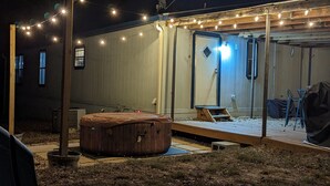 A backyard with a hot tub, string lights, and a wooden deck. - $0 Cleaning - Best for Groups and Families (Bastrop)