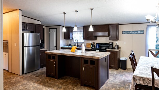 A kitchen with a central island, stainless steel refrigerator, dark wooden cabinets, and pendant lighting. - $0 Cleaning - Best for Groups and Families (Bastrop)