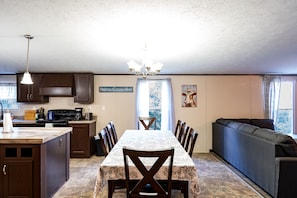 A spacious kitchen with dark wooden cabinets, a central island with a sink, and a dining area with a long table and chairs.